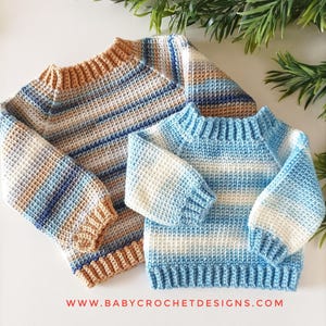 Peut inclure: Deux pulls crochetés à la main. L'un est de plus grande taille avec des rayures beiges, bleues et blanches. L'autre est de plus petite taille avec des rayures bleues et blanches. Les pulls ont des poignets et des cols côtelés. Le site web www.babycrochetdesigns.com est visible.
