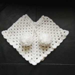 K&ouml;nnte beinhalten: Wei&szlig;es H&auml;kelponcho mit zwei wei&szlig;en Bommeln.