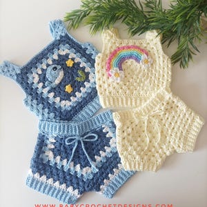 May include: Crocheted baby outfits in blue and cream. One set features a whale and stars, the other a rainbow and flowers. The shorts have a drawstring. The website address www.babycrochetdesigns.com is visible.