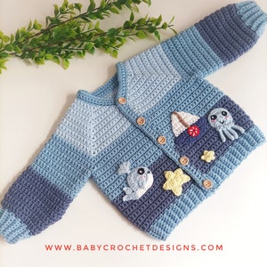 Op de afbeelding: Een blauwe en grijze gestreepte babytrui met gebreide octopus, zeilboot en ster applicaties. De trui heeft houten knopen en de tekst "www.babycrochetdesigns.com" is onderaan gedrukt.
