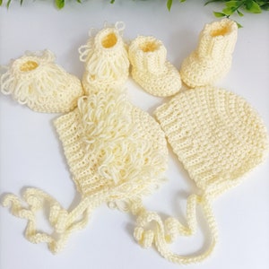 Puede incluir: Un conjunto de ropa de bebé de ganchillo en color amarillo pálido. El conjunto incluye un gorro, botines y un gorro con una larga corbata.