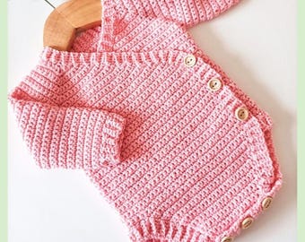 May include: A light pink long-sleeved crochet romper featuring a wrap-style front with four wooden buttons along the side and three wooden buttons at the bottom. The text reads Little Wrap Romper PDF Crochet Pattern By Baby Crochet Designs.