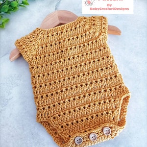 Peut inclure: Un body bébé crocheté de couleur jaune moutarde avec un motif délicat en point ajouré. Le body a trois boutons en bois en bas.