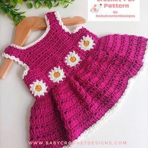May include: A pink crochet baby dress with white daisy accents and a white crocheted trim. The dress is on a wooden hanger. The text "Crochet PDF Pattern By BabyCrochetDesigns" is in the top right corner of the image. The text "www.babycrochetdesigns.com" is at the bottom of the image.