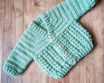 May include: A green crocheted baby cardigan with wooden buttons.
