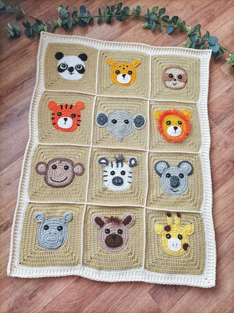 Peut inclure: Une couverture b&eacute;b&eacute; en crochet avec une vari&eacute;t&eacute; de visages d'animaux, dont un panda, un tigre, un singe, un z&egrave;bre et une girafe. La couverture est faite de fil beige et blanc et a une bordure blanche.