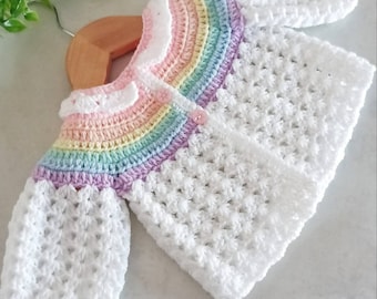 May include: A white crochet baby cardigan with a rainbow stripe across the shoulders. The cardigan has a button closure and a white crocheted collar.