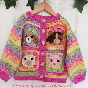 May include: A colourful crocheted cardigan with a rainbow stripe pattern and animal appliques. The cardigan has a pink background with a row of buttons down the front. The animal appliques are a dog, a horse, a llama, and a pig.