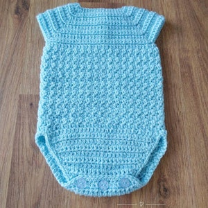 May include: A light blue crocheted baby onesie with short sleeves and snap closures. The onesie is made with a textured stitch and has a simple design.
