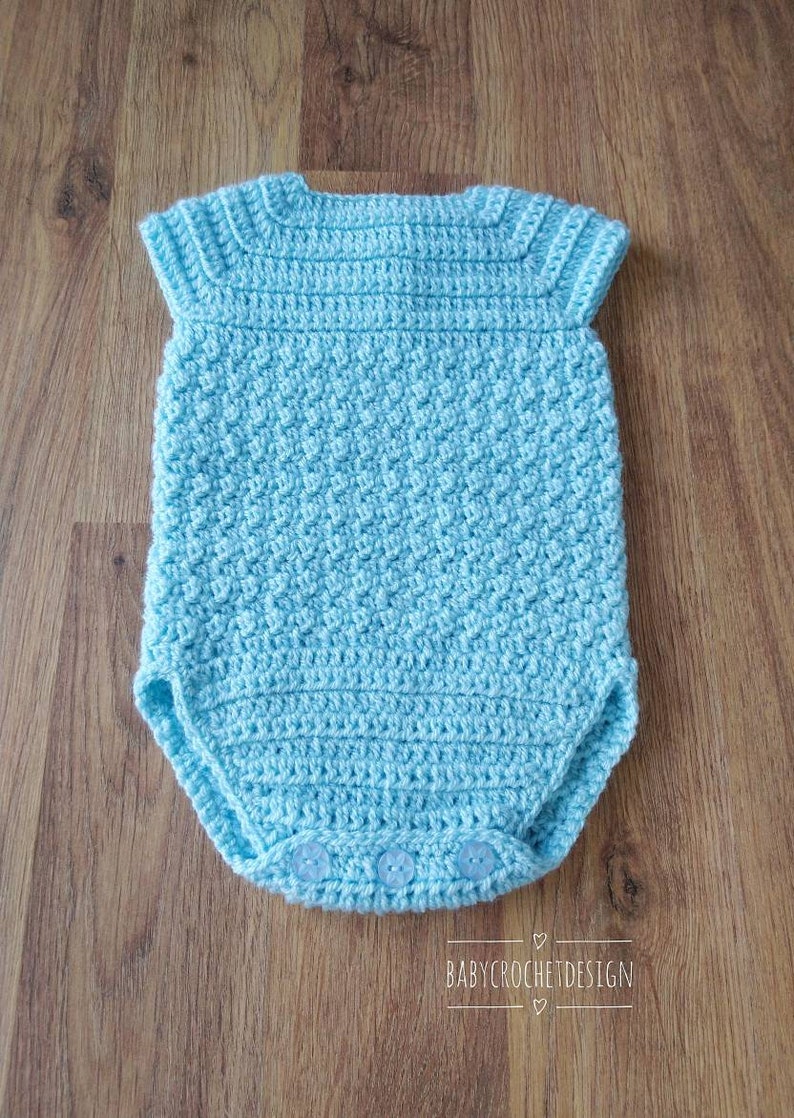 May include: A light blue crocheted baby onesie with short sleeves and snap closures. The onesie is made with a textured stitch and has a simple design.