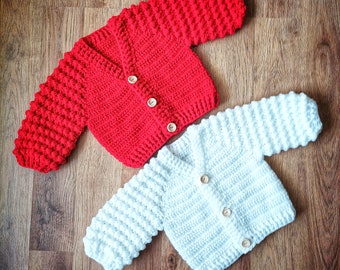 May include: Two crocheted baby cardigans, one red and one white, with wooden buttons.