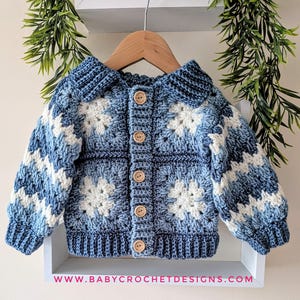 Puede incluir: Un cárdigan de bebé hecho a mano en tonos azules y blancos, con un diseño de cuadrados de la abuela. El suéter de ganchillo tiene cuello y se abrocha con botones de madera. La dirección del sitio web www.babycrochetdesigns.com es visible en la parte inferior.