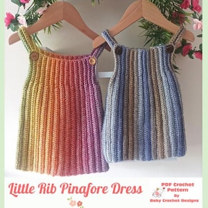 Peut inclure: Deux robes chasubles crochetées suspendues à des cintres en bois. La robe de gauche présente un motif côtelé vertical avec un dégradé de vert, jaune, orange et rose. La robe de droite a un dégradé de bleu, gris et marron. Texte : Little Rib Pinafore Dress.