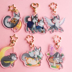 May include: Six colourful acrylic keychains featuring cartoon wolf characters. Each keychain has a different design, including a wolf with wings, a wolf sleeping on a crescent moon, and a wolf holding a teacup.