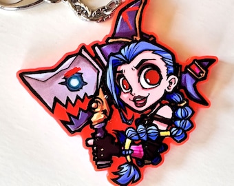 May include: A red, white, and blue keychain featuring a cartoon character with blue hair and a red and white hat holding a weapon. The character has one red eye and one blue eye.