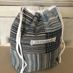 Könnte beinhalten: Eine blaue und weiße gestreifte Kordeltasche aus Stoff mit einem Patch, auf dem "LOVE IS THE ANCHOR" steht.