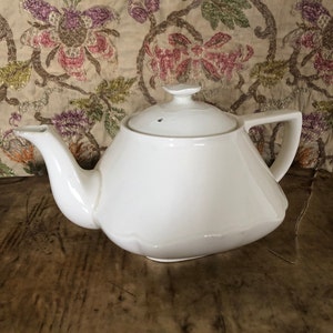 Könnte beinhalten: Eine weiße Teekanne aus Keramik mit quadratischem Boden und Deckel. Die Teekanne hat einen Ausguss und einen Griff.