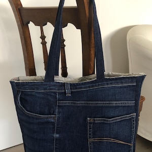 Könnte beinhalten: Eine dunkelblaue Jeans-Tragetasche mit weißem Blumenfutter. Die Tasche hat zwei große Taschen auf der Vorderseite und eine kleinere Tasche auf der Rückseite. Die Tasche hat einen braunen Leder-Patch mit dem Text "LIFE FOR THE UNIQUE HANDBAGS".