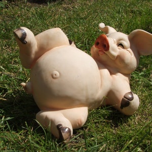 May include: A pink ceramic pig figurine lying on its back with its legs in the air. The pig has a brown snout and hooves.