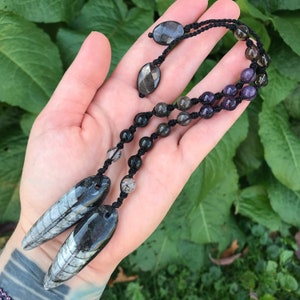 May include: A black cord necklace with a variety of gemstone beads, including amethyst, clear quartz, and black onyx. The necklace has two black and white fossil pendants at the end.