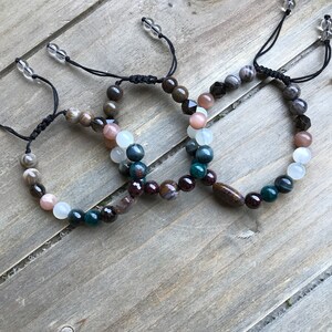 May include: Three beaded bracelets with brown, white, green, and black beads. The bracelets are made with natural stones and have adjustable cords.