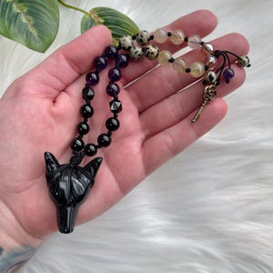 Puede incluir: Collar con colgante de lobo de ónix negro con cuentas de ónix negro, cuentas de amatista, cuentas de jaspe dálmata y cuentas de cuarzo transparente. El collar también incluye un dije de llave dorado.