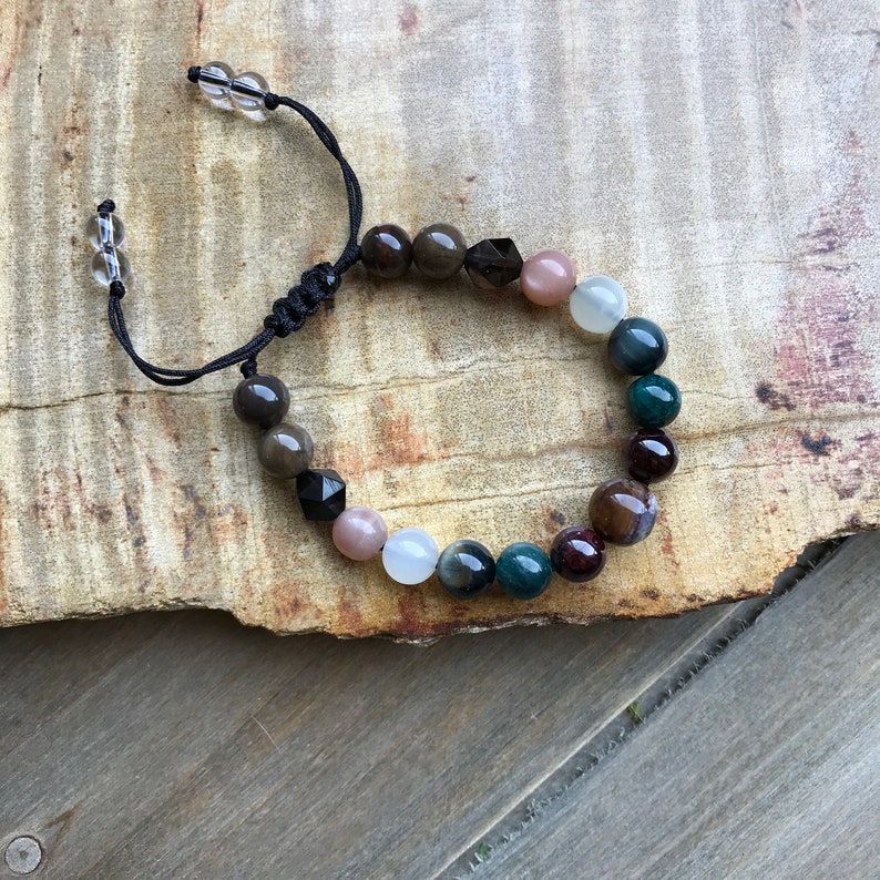 May include: A beaded bracelet with a black cord and a variety of gemstone beads, including brown, black, white, green, and red.