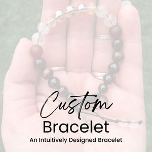 May include: A custom bracelet with a variety of stones, including clear quartz, tiger's eye, and red jasper. The bracelet is tied with a black cord and has a knot at the end. The text "Custom Bracelet" and "An Intuitively Designed Bracelet" is printed below the bracelet.