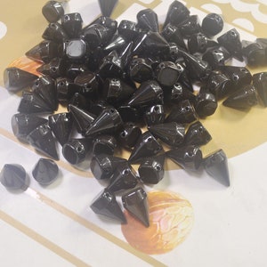 May include: A large quantity of black, pointy, plastic studs. The studs are all the same size and shape, and they are arranged in a random pattern.
