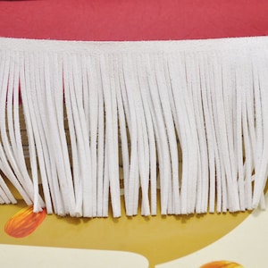 May include: White leather fringe trim with a soft texture. The fringe is approximately 1 inch long.