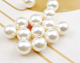 May include: A group of white pearl beads with gold accents. The beads are arranged in a cluster on a striped surface.