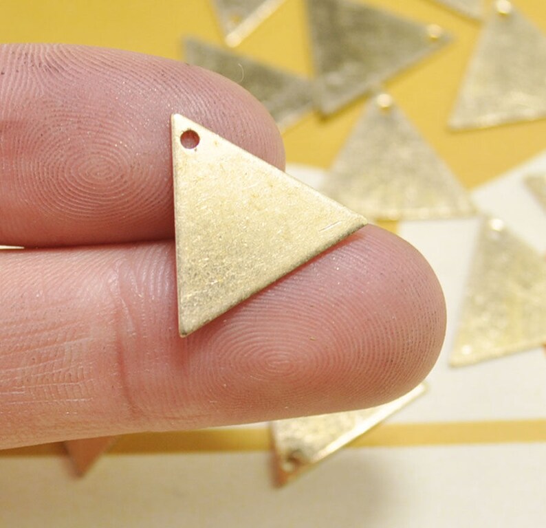 May include: A close-up of a gold triangle pendant with a small hole at the top. The pendant is made of metal and has a textured surface.