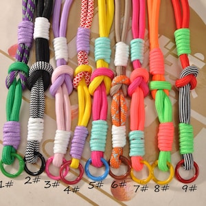 May include: A selection of brightly coloured lanyards. Each lanyard displays a unique colour combination, such as purple, black, pink, yellow, orange, and red. Each lanyard has a metal ring at the base and is numbered.