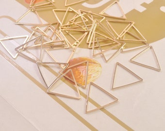May include: A large quantity of gold-colored metal triangle shapes. The triangles are all the same size and shape, and they are scattered randomly on a white surface.