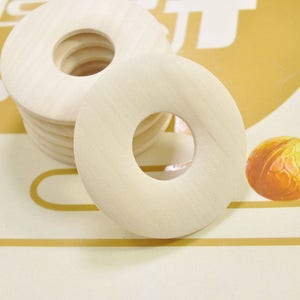 Pode incluir: Uma pilha de anéis de madeira com um furo no centro. Os anéis são de cor castanho claro e têm um acabamento liso e polido.