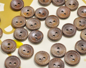 Könnte beinhalten: Eine Sammlung brauner Holz-Knöpfe mit zwei Löchern und einem dekorativen weißen Rand. Die Knöpfe sind in einem zufälligen Muster auf einer weißen Oberfläche angeordnet.