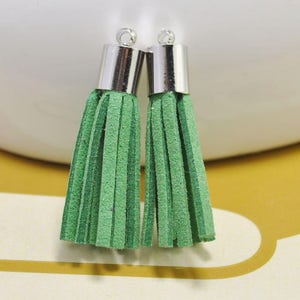 Könnte beinhalten: Zwei grüne Samtquasten mit silbernen Metallkappen. Die Quasten sind etwa 5 cm lang.