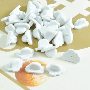 May include: A pile of white plastic pin back closures for badges or buttons. The closures are shaped like a cloud with a small hole in the centre.