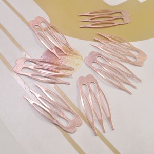 May include: Several rose gold hair combs are scattered across a light-colored surface. Each comb features a unique design with multiple tines and decorative cutouts. The combs are made of a metallic material and appear to be new.