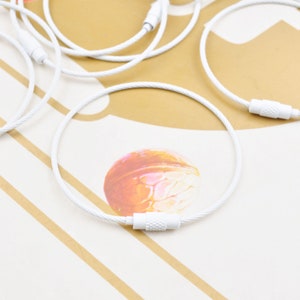 Könnte beinhalten: Weiße Kabelbinder mit einem Metallverschluss. Die Kabelbinder sind geschlungen und auf einer weißen und braunen Oberfläche angeordnet.