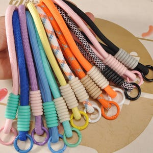 Puede incluir: Una colección de cordones coloridos en varios tonos, incluyendo rosa, azul, morado y naranja. Cada cordón presenta un diseño de cuerda con un anillo en el extremo. Los cordones están diseñados para sujetar llaves u otros objetos pequeños.