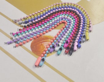 May include: A set of 13 colourful metal chains with numbered tags. The chains are made of small, round beads and are available in a variety of colours, including pink, blue, purple, and green.