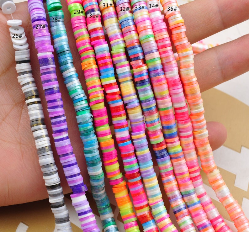 Pu&ograve; includere: Primo piano di 10 fili di perline di ceramica rotonde, piatte e colorate. Le perline sono disposte in fila, con ogni filo numerato da 26 a 35. Le perline sono un mix di colori vivaci, tra cui rosa, blu, verde, giallo e viola.