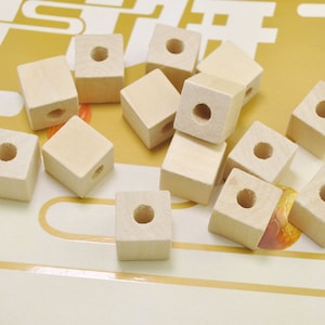 May include: A group of 13 unfinished wooden cubes with a hole drilled through the center of each cube. The cubes are scattered on a yellow surface.
