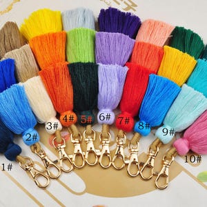 May include: Ten colourful tassel keychains with gold metal clasps. The tassels are in various colours, including blue, green, red, yellow, and pink. Each tassel is numbered from 1 to 10.