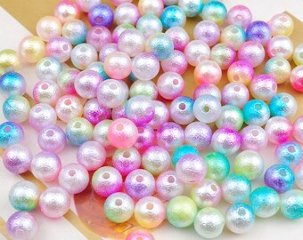 May include: A large pile of iridescent pearl beads in various pastel colors, including pink, blue, green, and yellow. The beads are round and have a smooth, slightly textured surface.