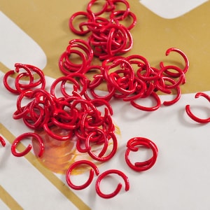 Puede incluir: Un montón grande de anillos de salto de metal rojo. Los anillos son todos del mismo tamaño y están dispuestos en un patrón aleatorio.