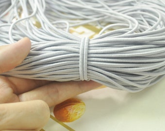 May include: A large spool of light grey elastic string. The string is tightly wound and appears to be very stretchy.