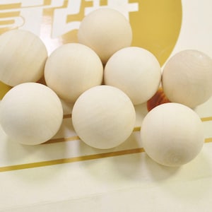 Puede incluir: Ocho bolas de madera blancas, dispuestas en círculo sobre una superficie rayada dorada y blanca.