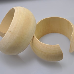 Può includere: Due braccialetti in legno non finiti, uno è più largo dell'altro, entrambi sono di colore marrone chiaro.